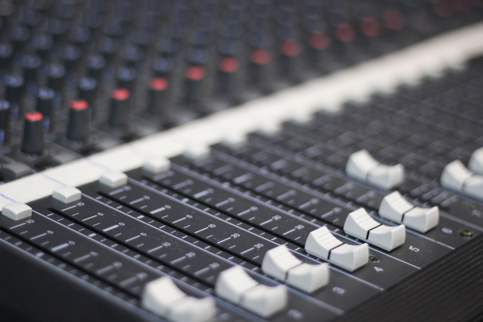 Mesa de som com faders e botões em close, canais de mixagem em destaque